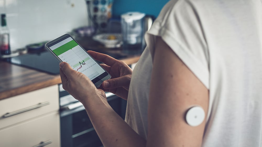 Woman checking glucose level with a remote sensor and mobile phone.